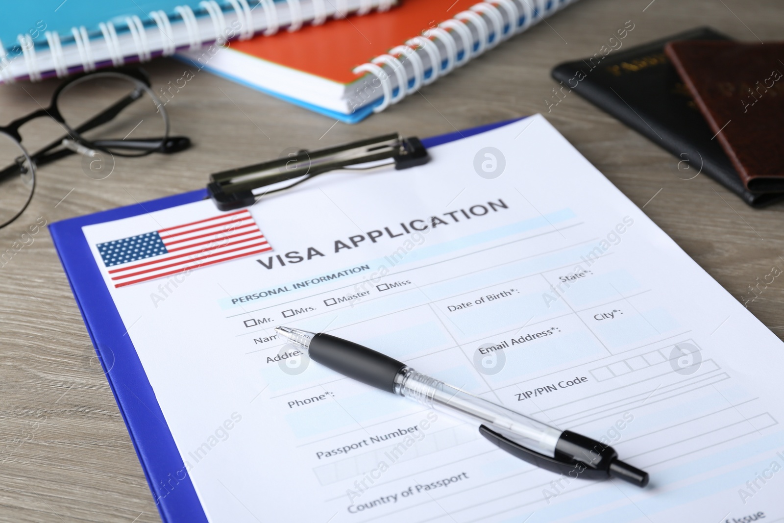 Photo of Visa application form for immigration to USA and pen on wooden table, closeup