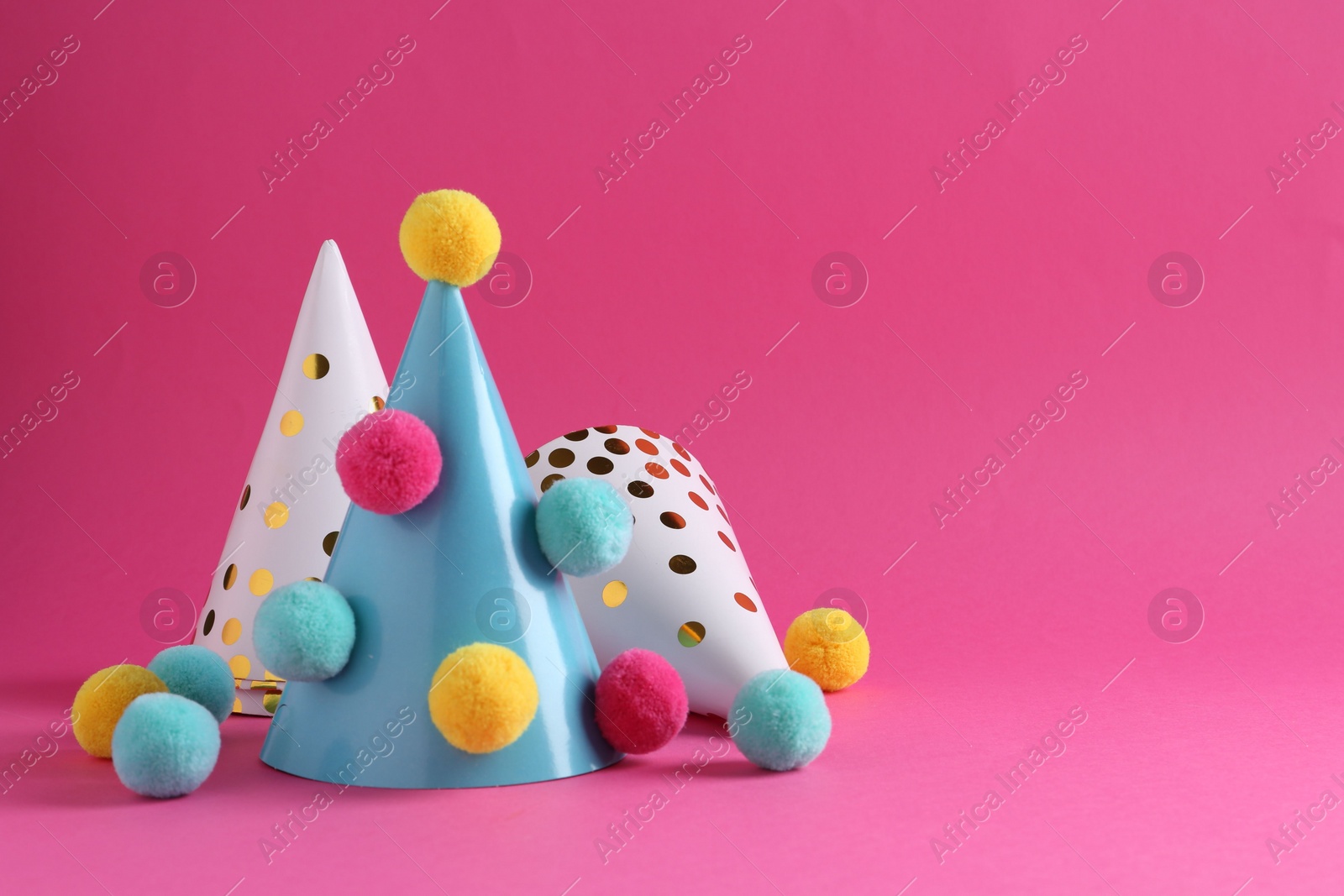 Photo of Party hats with color pompoms on pink background, space for text