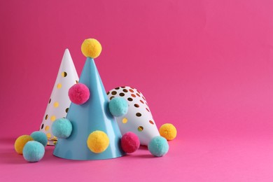 Photo of Party hats with color pompoms on pink background, space for text