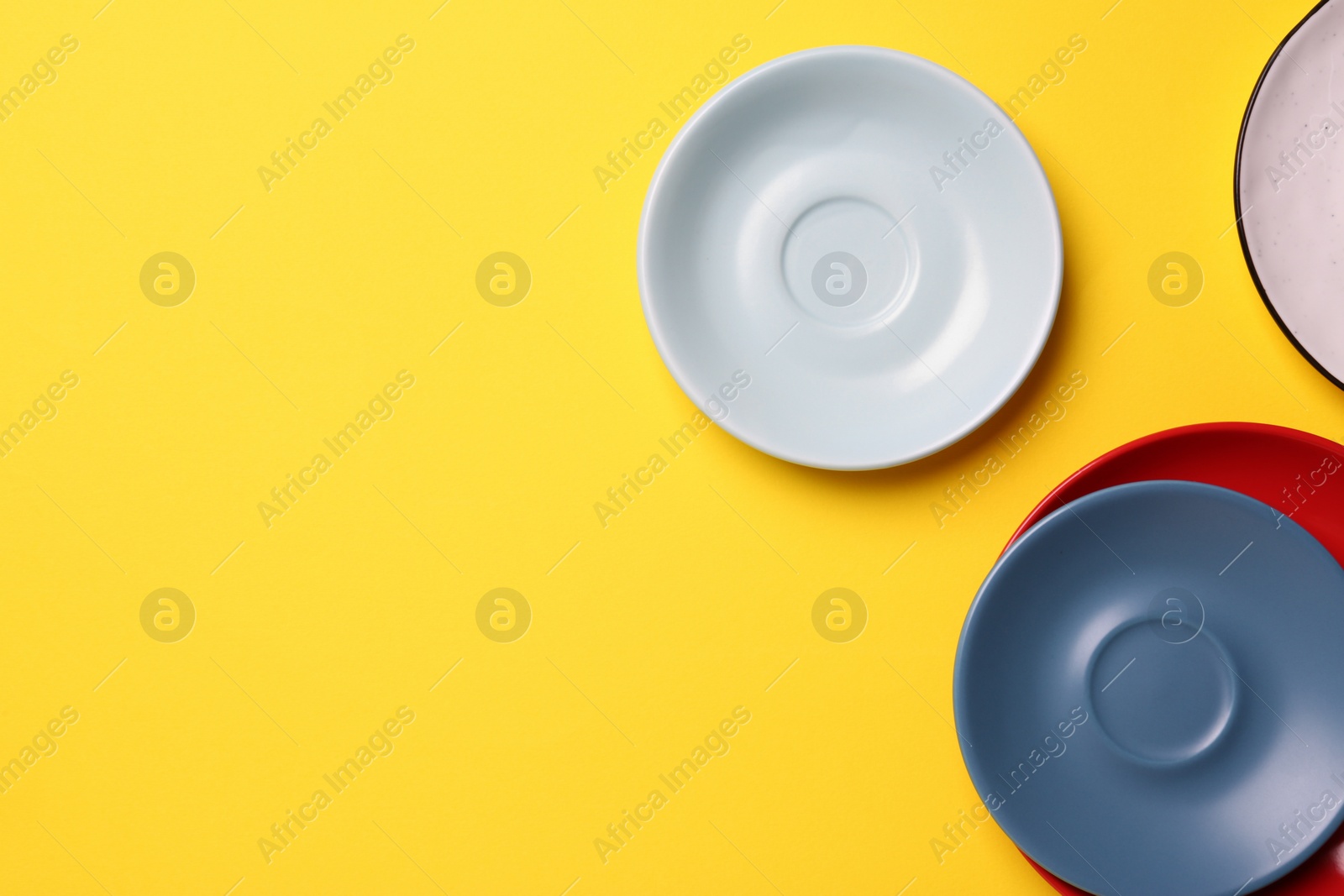 Photo of Clean ceramic plates on yellow background, flat lay. Space for text