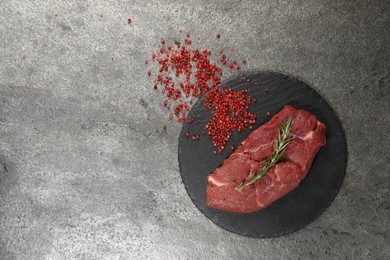 Photo of Piece of raw beef meat, rosemary and red peppercorns on grey table, flat lay. Space for text