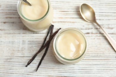 Jars with vanilla pudding and sticks on wooden background