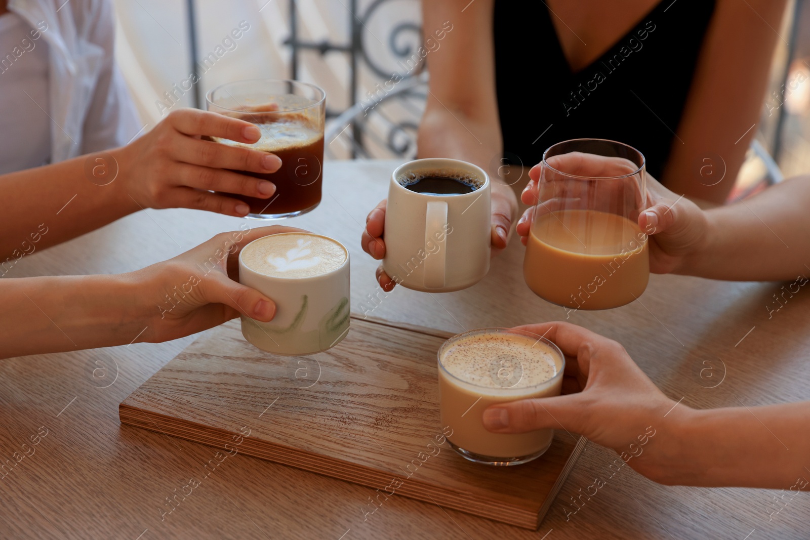 Photo of Friends drinking coffee at wooden table in cafe, closeup