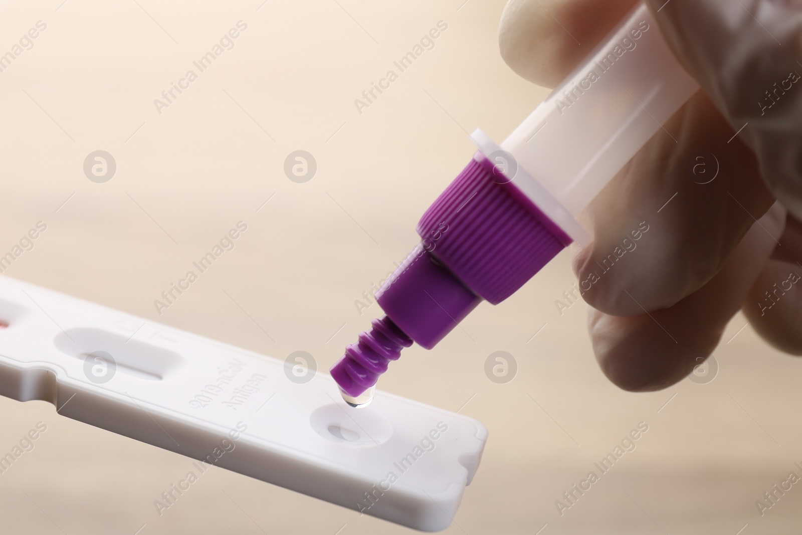 Photo of Doctor dropping buffer solution onto disposable express test cassette against blurred background, closeup