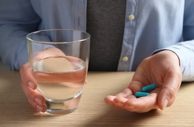 Photo of Woman with glass of water and pills at wooden table, closeup