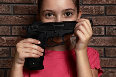 Photo of Little child playing with gun against brick wall. Dangerous game