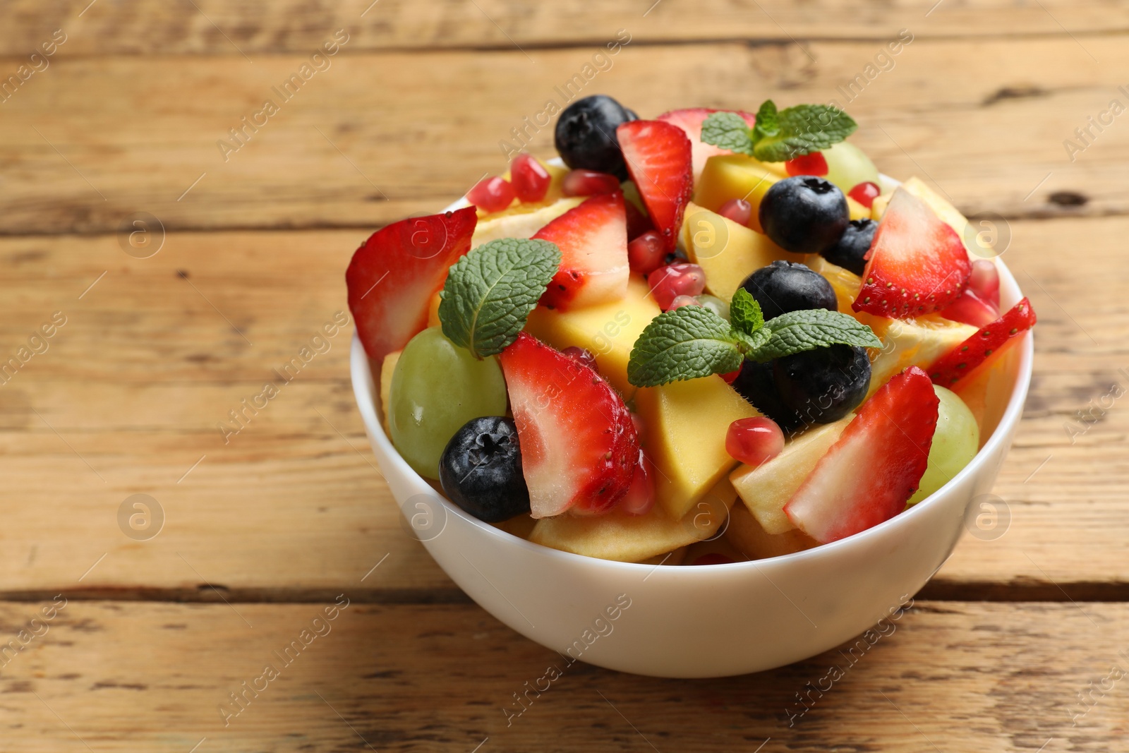 Photo of Tasty fruit salad in bowl on wooden table, closeup