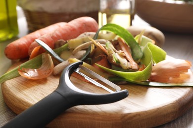 Peels of fresh vegetables and peeler on table, closeup