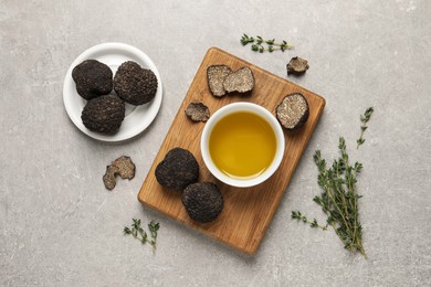 Photo of Fresh truffles, oil in bowl and thyme on light grey table, flat lay
