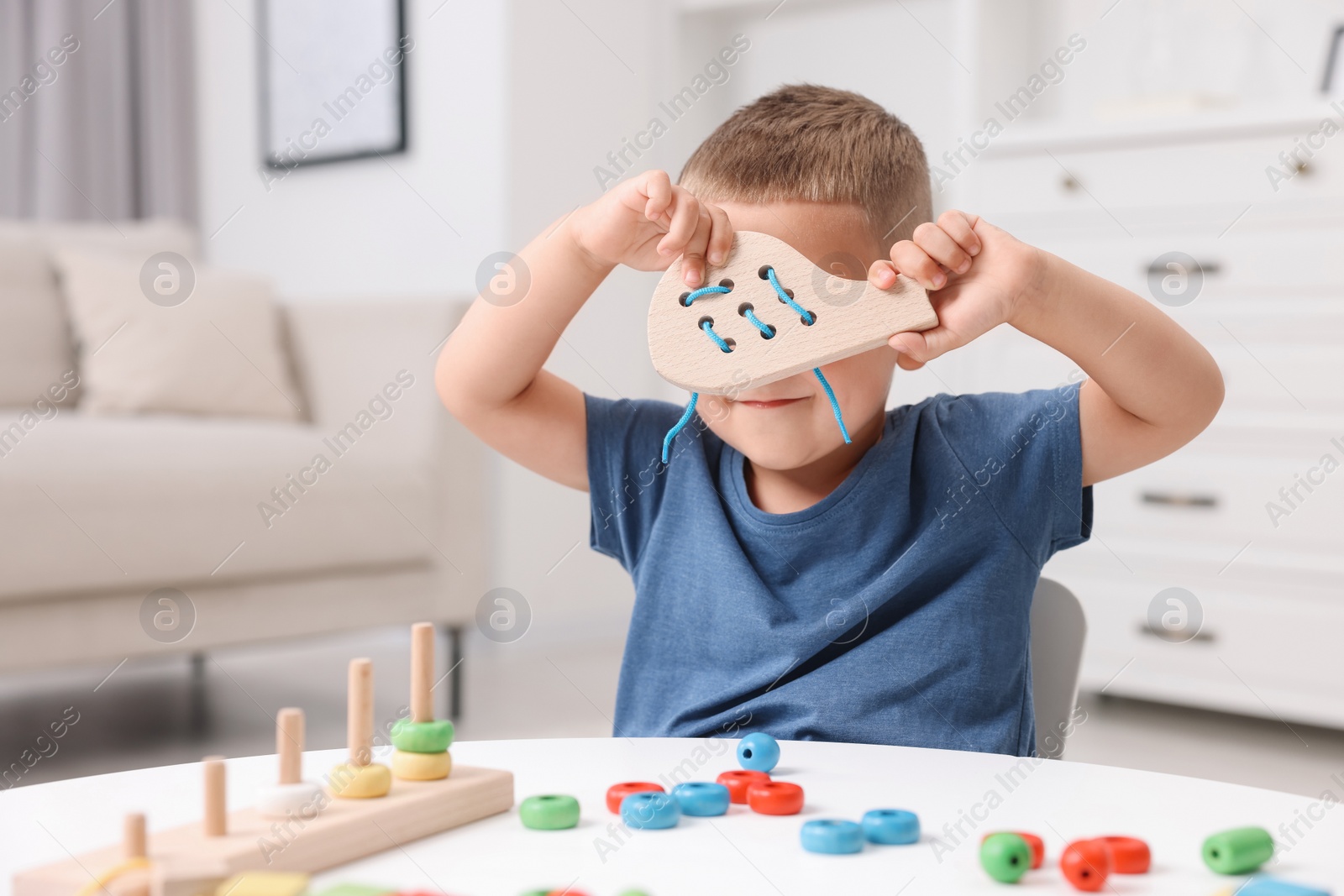 Photo of Motor skills development. Little boy playing with wooden lacing toy at white table indoors