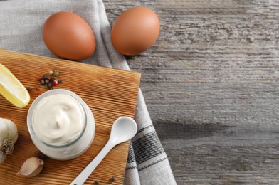 Photo of Fresh mayonnaise sauce in glass jar and ingredients on wooden table, flat lay. Space for text