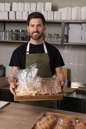 Happy seller with pastries at cashier desk in bakery shop