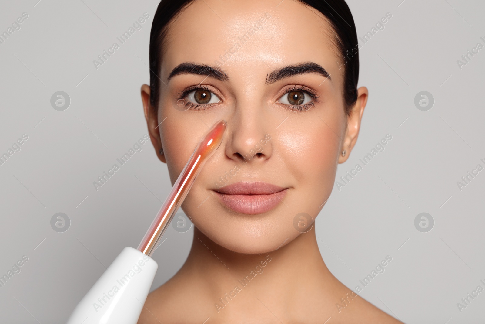 Photo of Woman using high frequency darsonval device on grey background