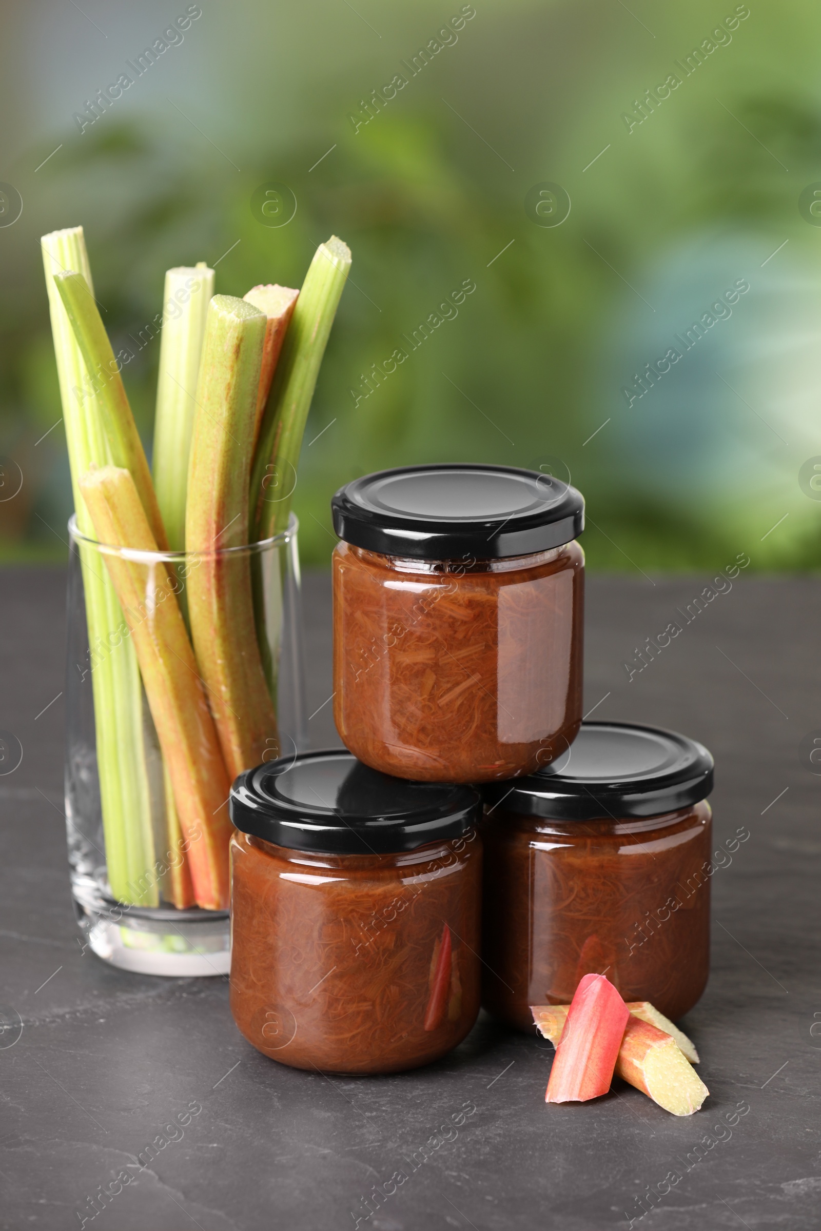 Photo of Jars of tasty rhubarb jam and stalks on grey table