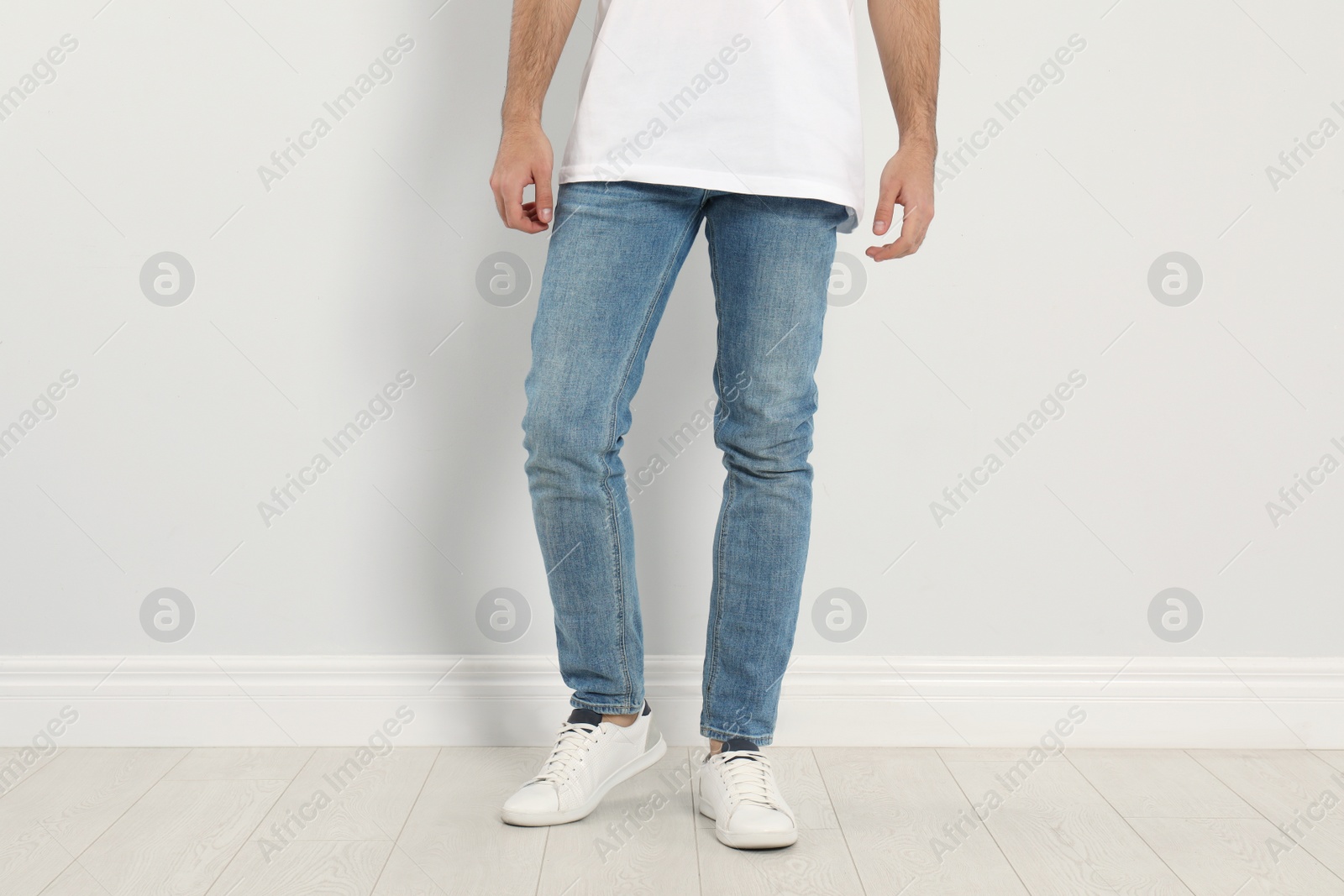 Photo of Young man in stylish jeans near light wall, closeup