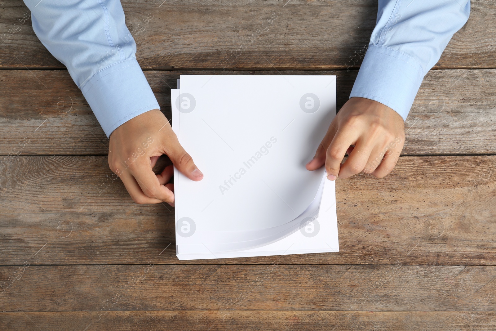 Photo of Man holding blank paper sheets for brochure at wooden table, top view. Mock up