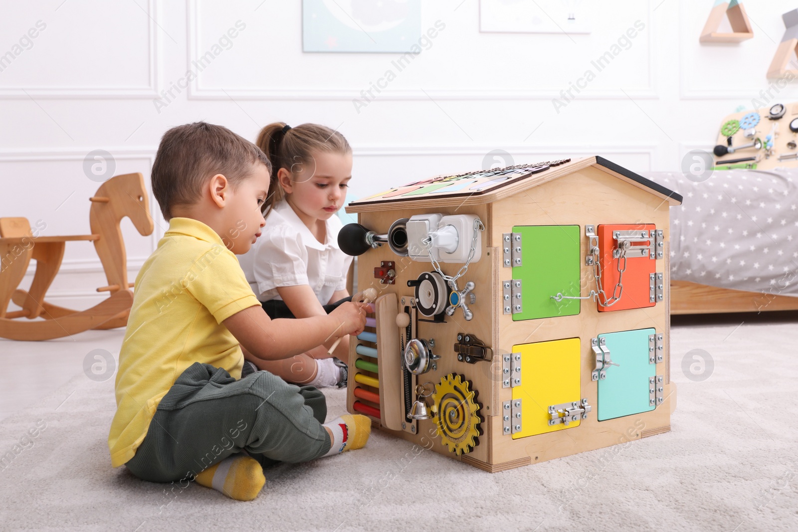 Photo of Little boy and girl playing with busy board house on floor in room