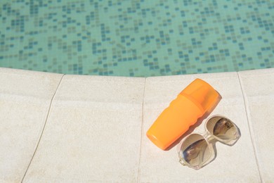Photo of Stylish sunglasses and sunscreen near outdoor swimming pool on sunny day, space for text. Beach accessories