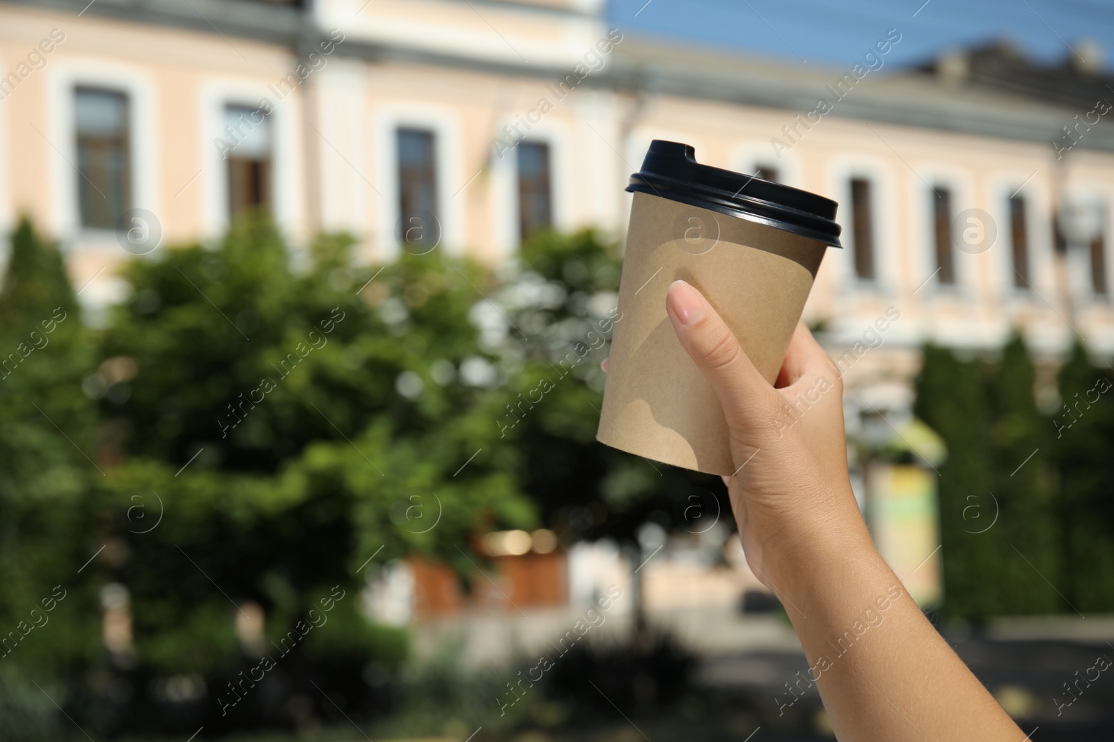 Photo of Woman holding takeaway cardboard coffee cup with plastic lid outdoors, closeup