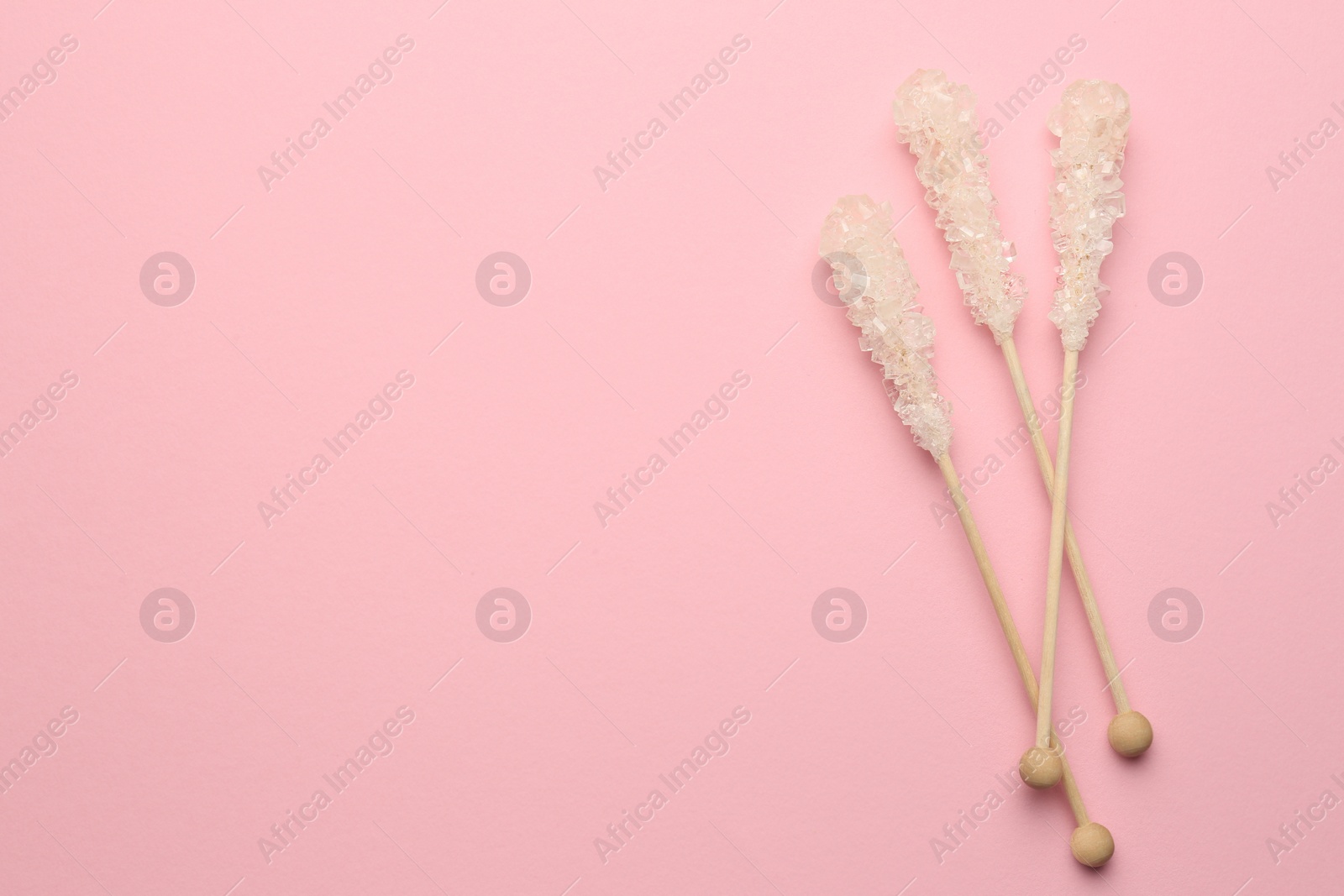 Photo of Wooden sticks with sugar crystals and space for text on pink background, flat lay. Tasty rock candies