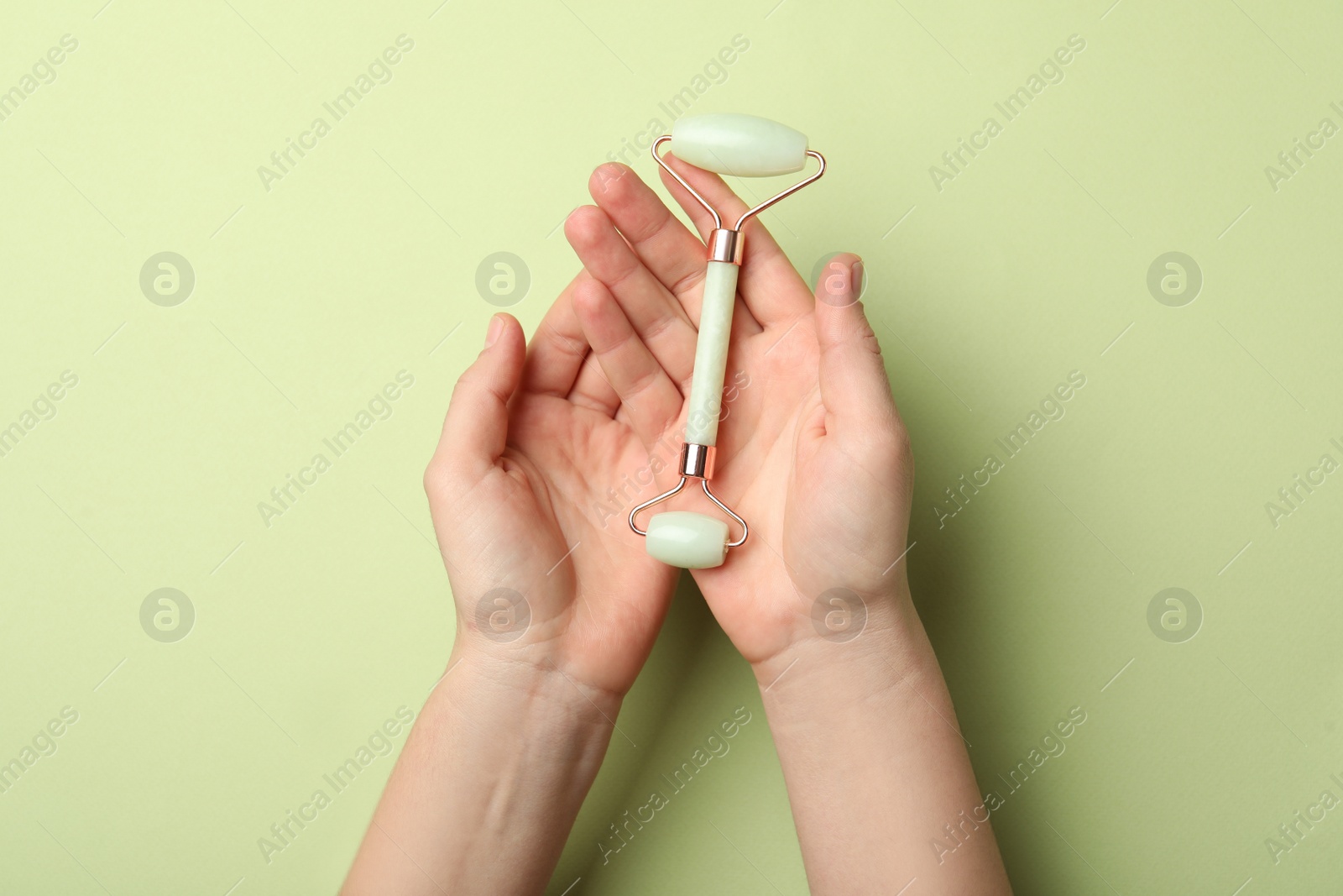 Photo of Woman with natural face roller on green background, top view