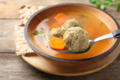 Photo of Spoon with matzoh ball over bowl of soup on table, closeup. Jewish cuisine