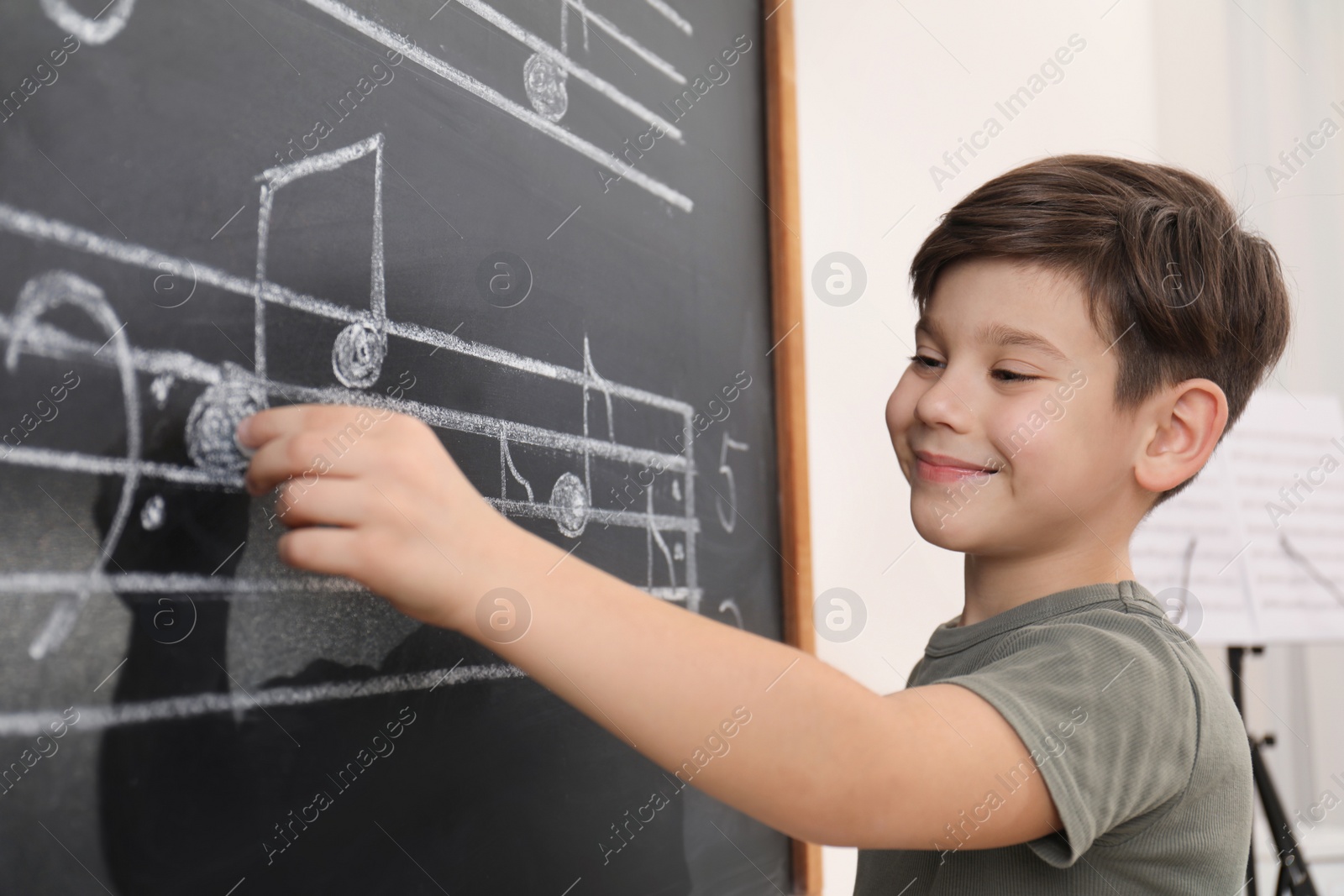 Photo of Little boy writing music notes on blackboard in classroom