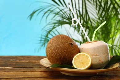 Plate with coconuts and lemon on wooden table against blue background. Space for text