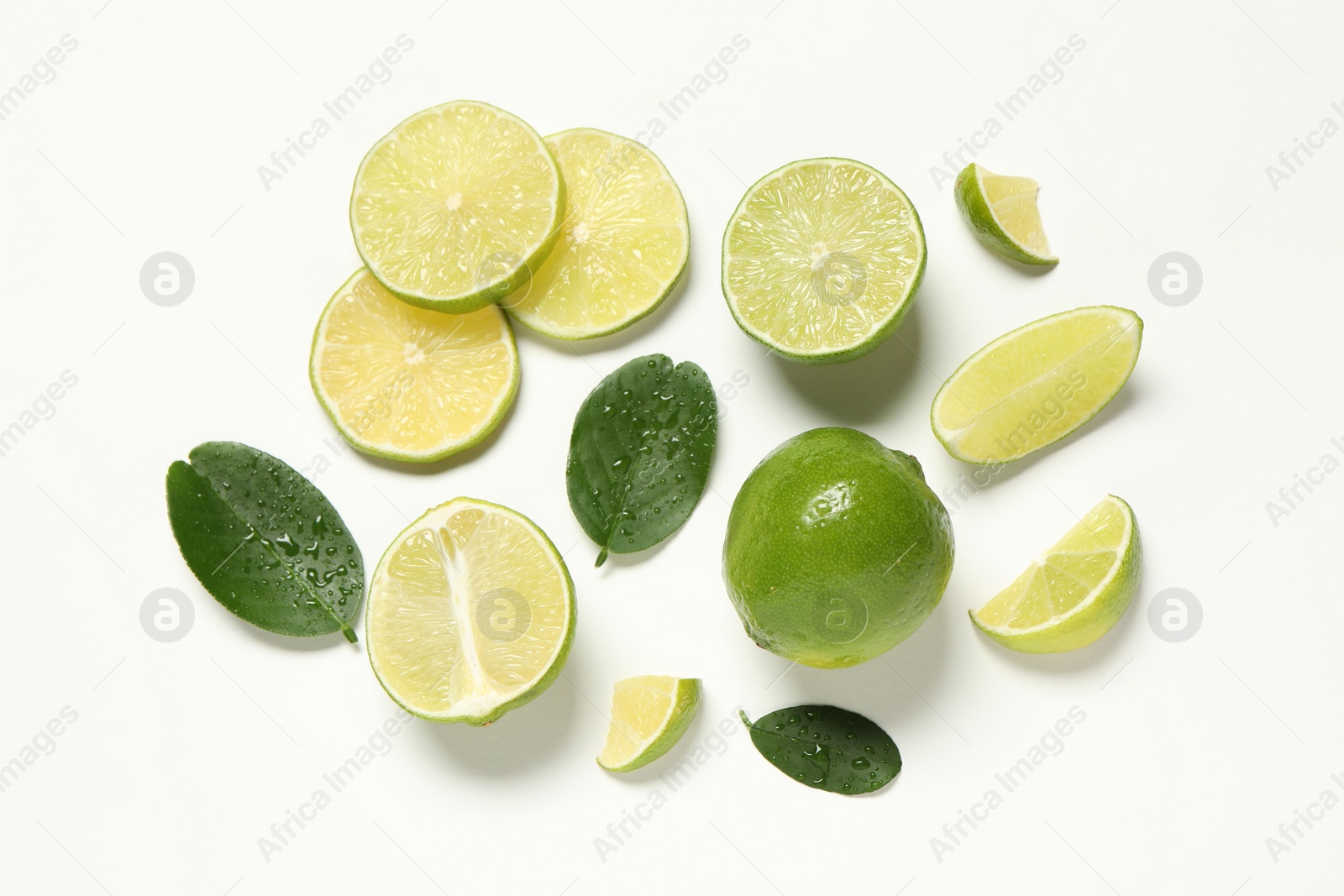 Photo of Whole and cut fresh ripe limes with green leaves on white background, flat lay