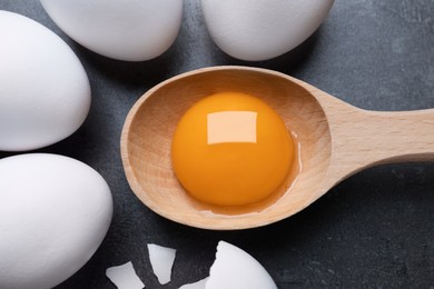 Raw chicken eggs and spoon with yolk on grey table, flat lay