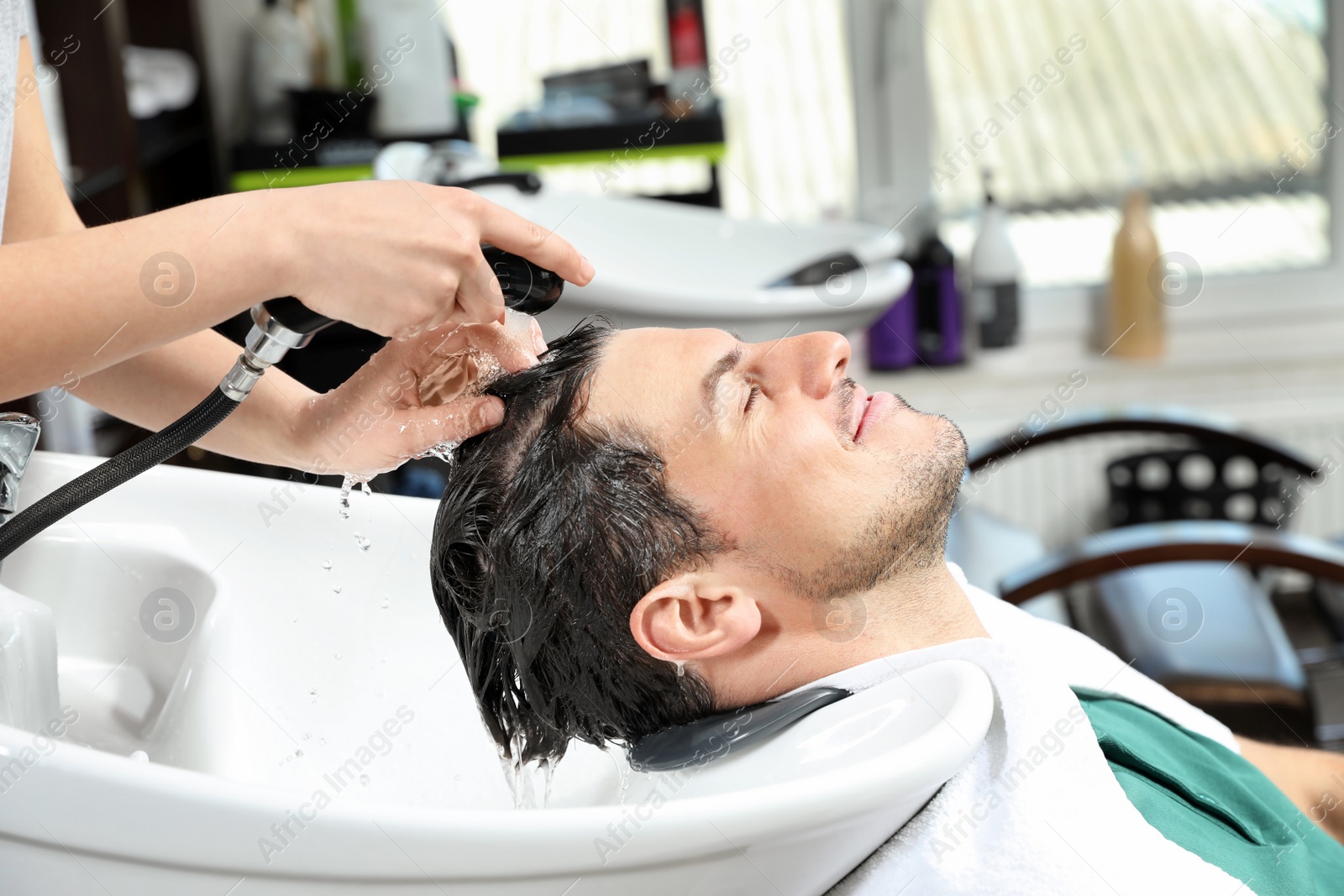 Photo of Stylist washing client's hair at sink in beauty salon