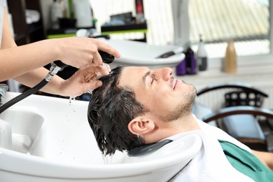 Stylist washing client's hair at sink in beauty salon