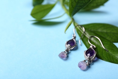 Photo of Beautiful pair of silver earrings with amethyst gemstones and leaves on light blue background, closeup. Space for text