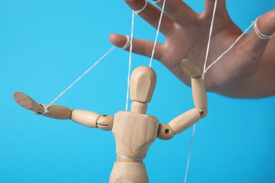 Woman pulling strings of puppet on light blue background, closeup