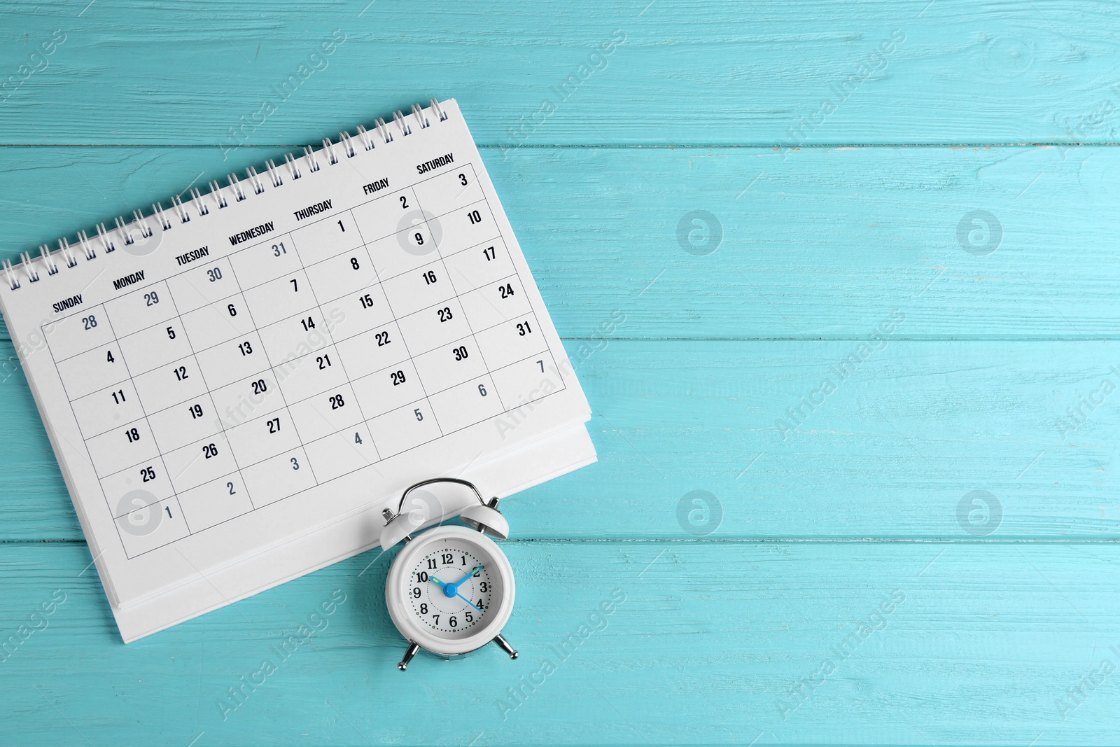 Photo of Calendar and alarm clock on light blue wooden background, flat lay. Space for text