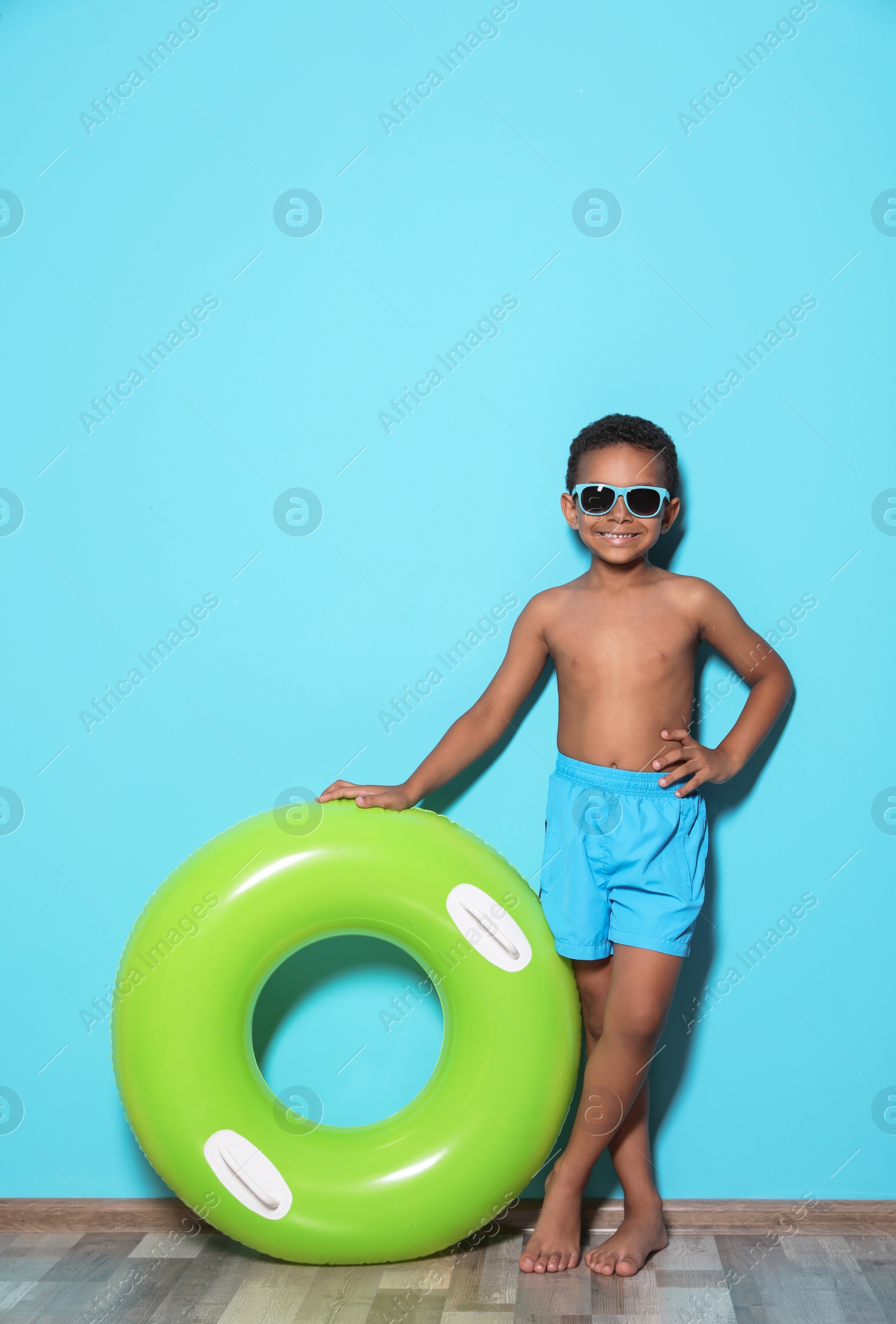 Photo of Cute African American boy with bright inflatable ring near color wall