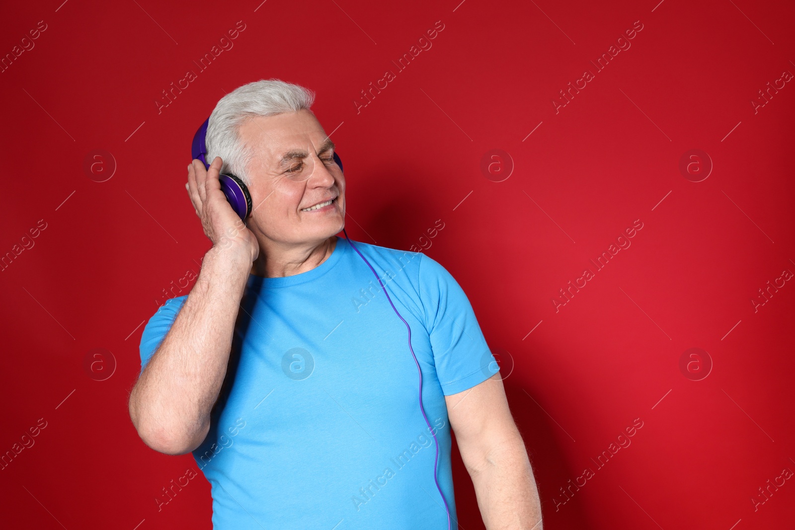 Photo of Mature man enjoying music in headphones on color background. Space for text