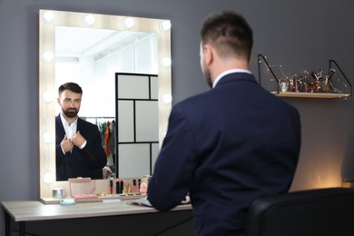 Photo of Young handsome man near mirror in makeup room