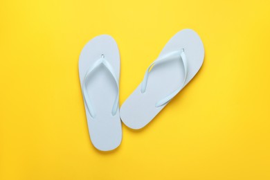 Stylish white flip flops on yellow background, top view