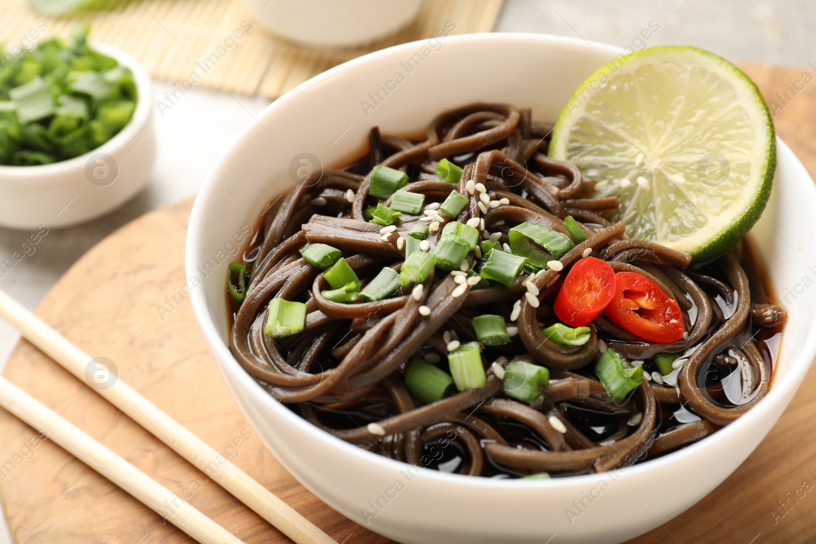 Photo of Tasty buckwheat noodles (soba) with sauce, onion in bowl and chopsticks on table, closeup