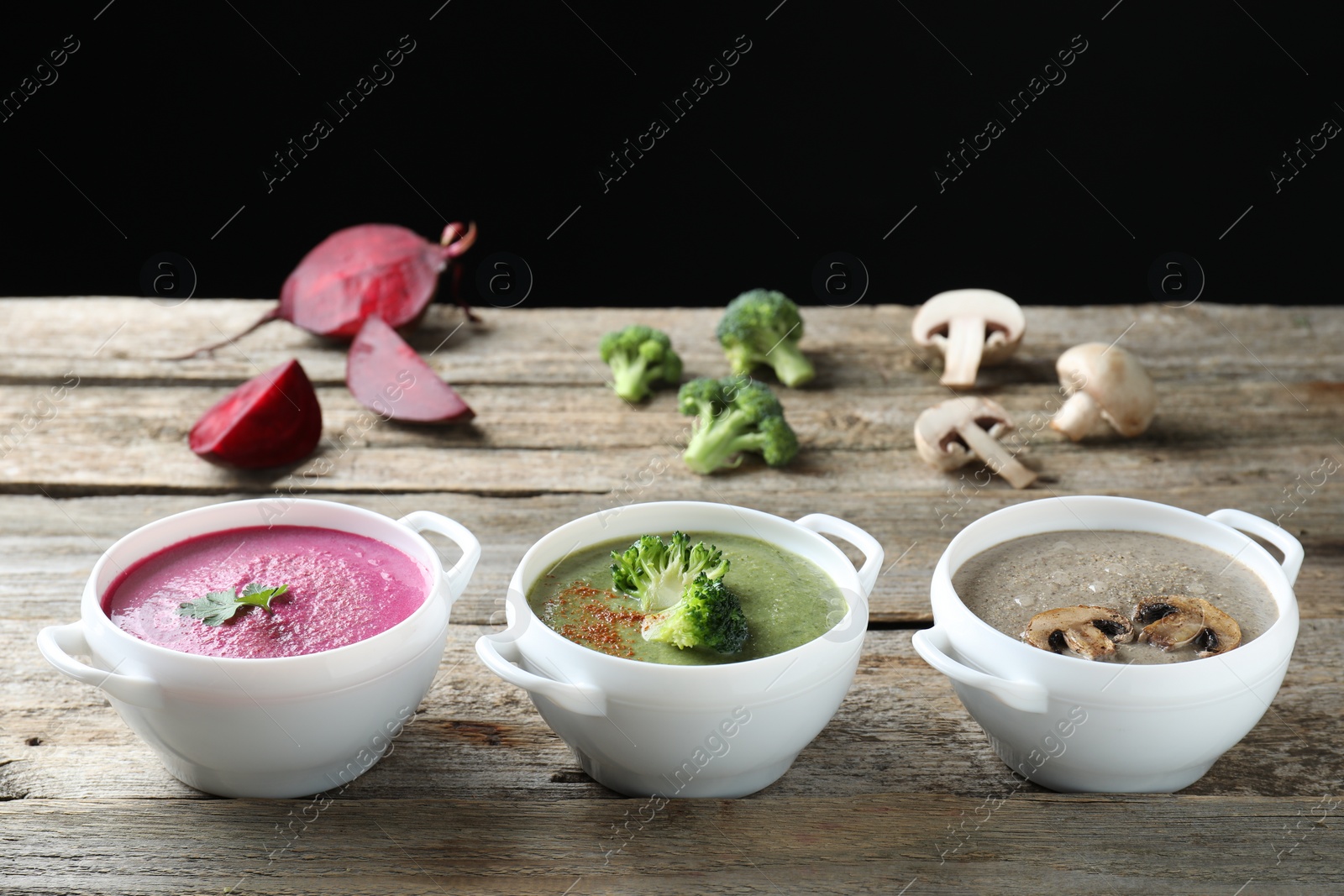 Photo of Different tasty cream soups in bowls and ingredients on old wooden table