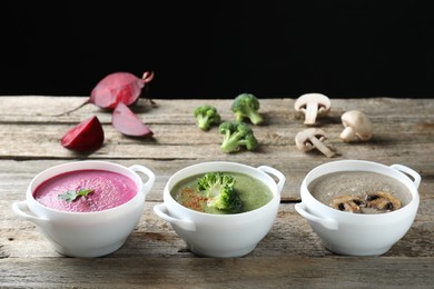 Different tasty cream soups in bowls and ingredients on old wooden table