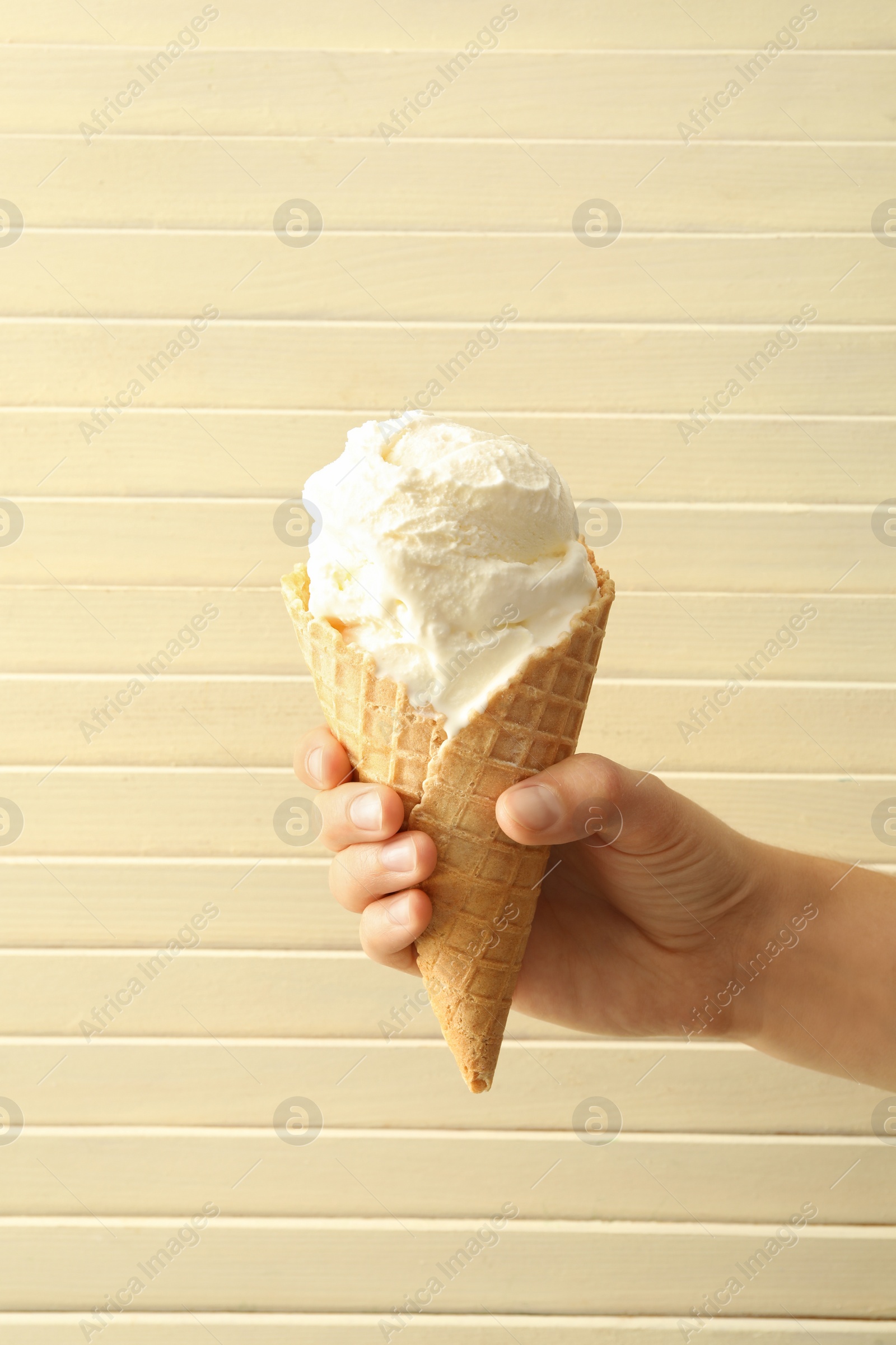 Photo of Woman holding waffle cone with delicious ice cream on wooden background, closeup