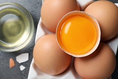 Photo of Box of whole and cracked chicken eggs on grey table, flat lay