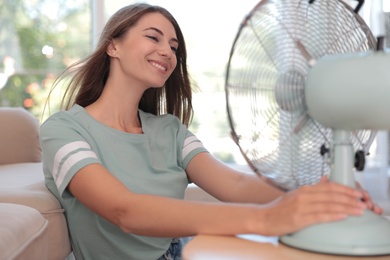 Woman enjoying air flow from fan in living room. Summer heat