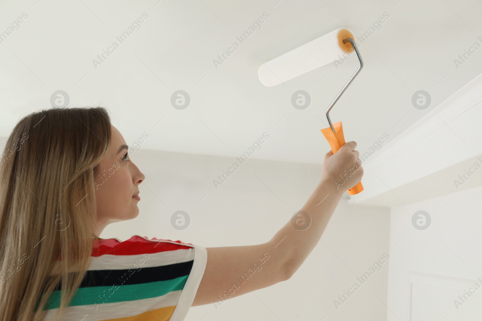 Photo of Young woman painting ceiling with white dye indoors