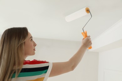 Young woman painting ceiling with white dye indoors