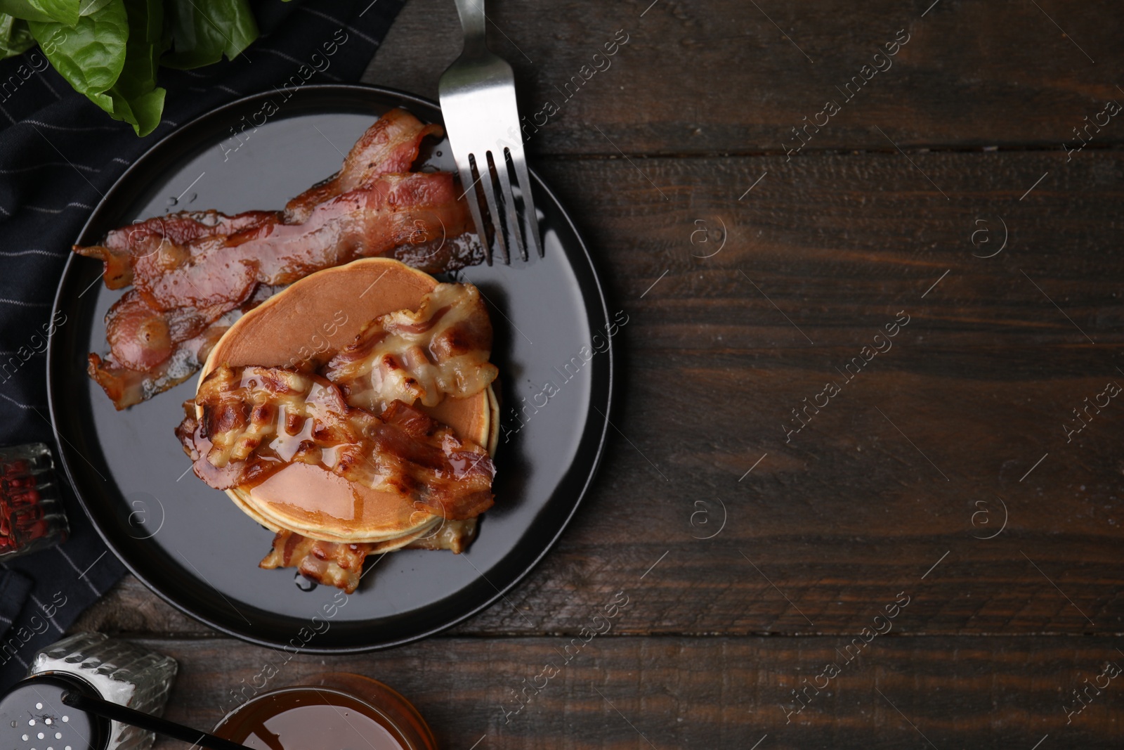 Photo of Delicious pancakes with fried bacon served on wooden table, flat lay. Space for text