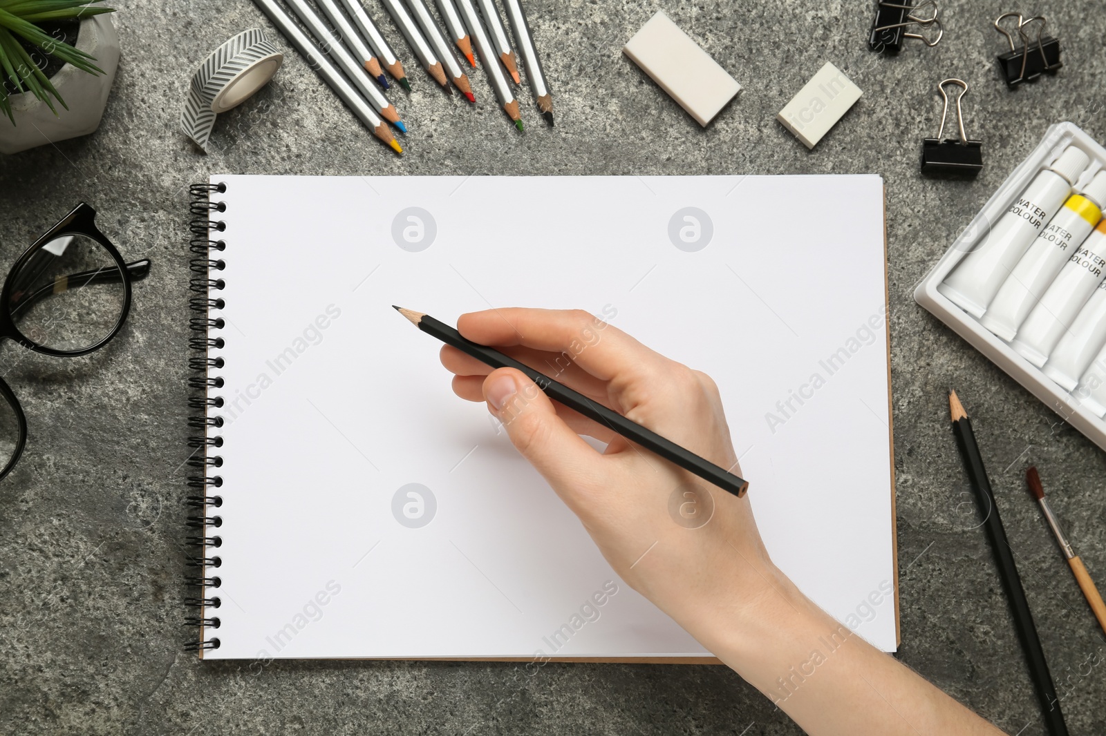 Photo of Woman with pencil and blank sketchbook at grey stone table, top view