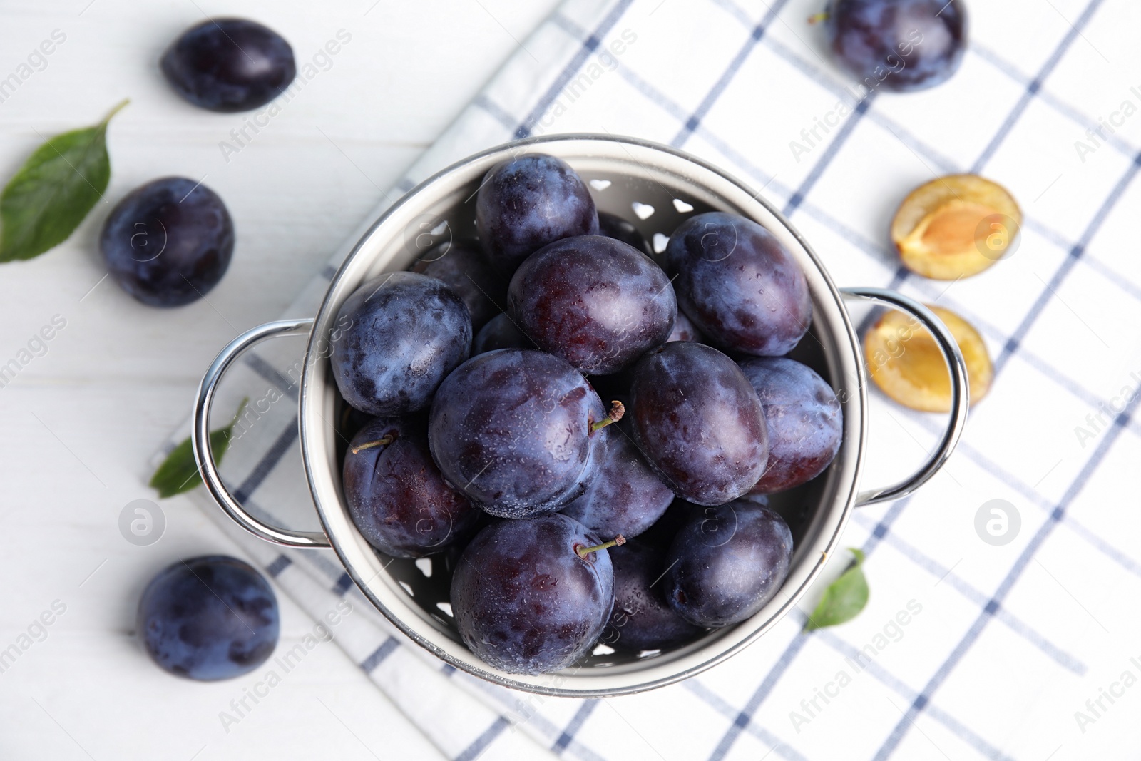 Photo of Delicious ripe plums in colander on white table, flat lay